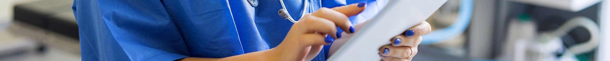 Eine Krankenschwester steht in einem Behandlungszimmer und tippt auf ein Tablet.