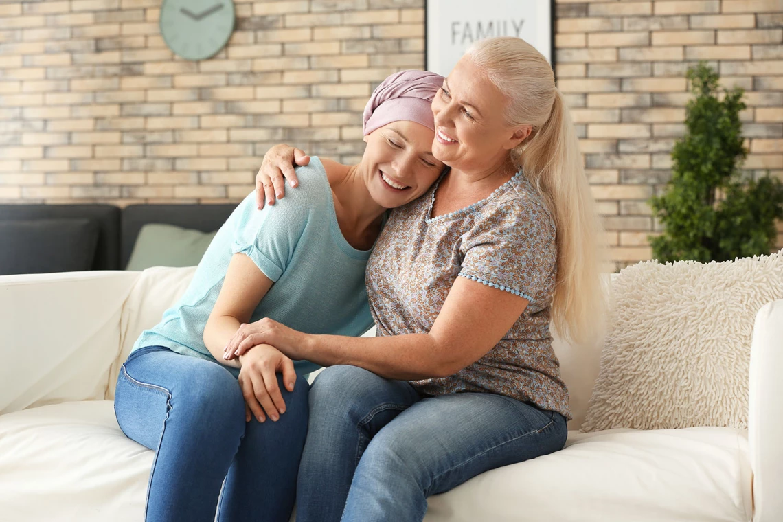 Eine Krebspatientin liegt lächelnd im Arm einer Frau.