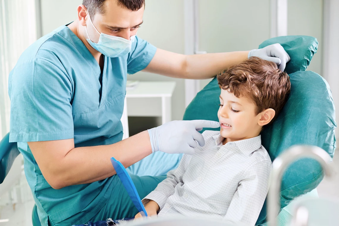 Ein Zahnarzt zeigt einem Jungen mit einem Spiegel in der Hand seine Zähne.