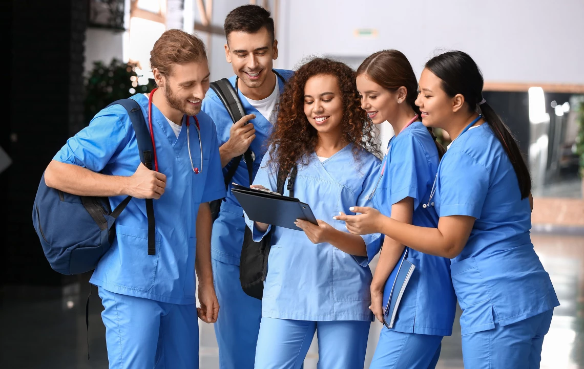 Fünf junge Ärzte schauen sich gemeinsam ein Dokument in der Hand der mittleren Person an.