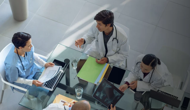 Fünf Ärzte sitzen um einen Glastisch während eines Meetings.