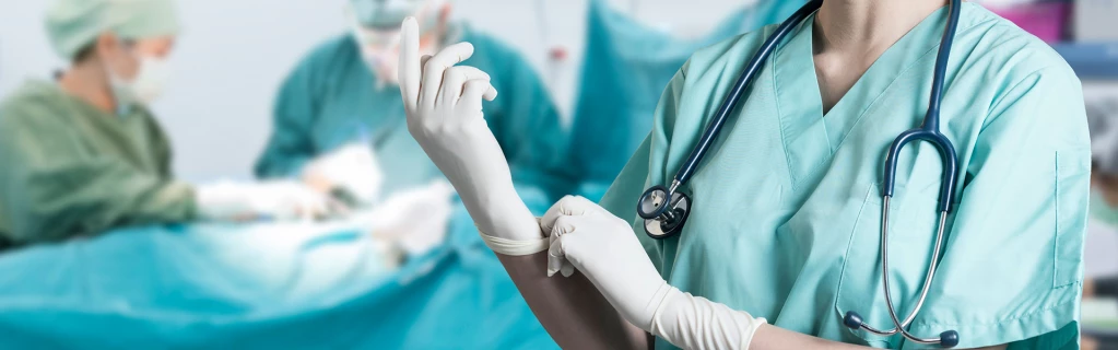 Eine Chirurgin setzt vor einem Operationstisch ihre Handschuhe auf.