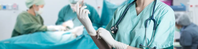 Eine Chirurgin setzt vor einem Operationstisch ihre Handschuhe auf.