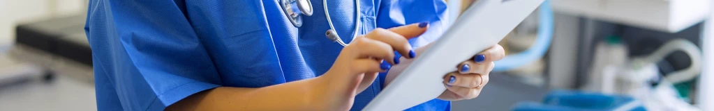 Eine Krankenschwester steht in einem Behandlungszimmer und tippt auf ein Tablet.