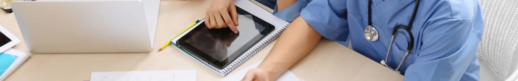 Medizinstudenten sitzen gemeinsam an einem Tisch und lernen mit Heftern und Laptops.