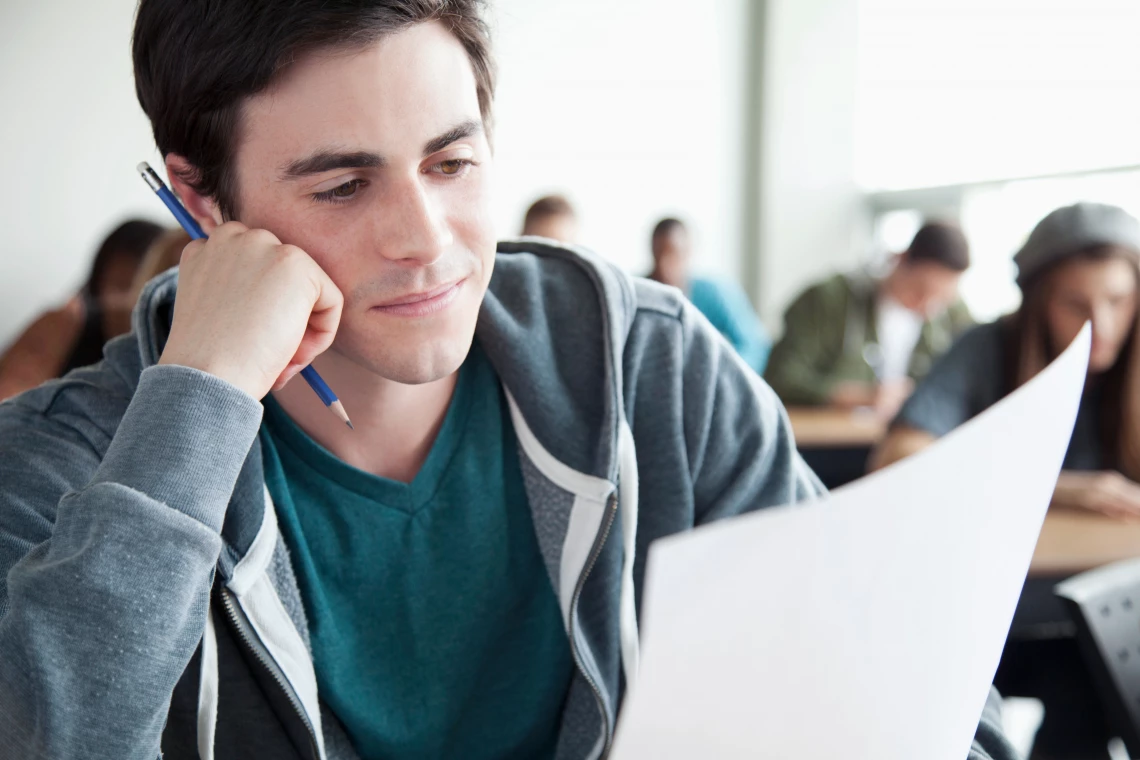 Ein Junge sitzt in einer Prüfung und schaut auf sein Aufgabenblatt.