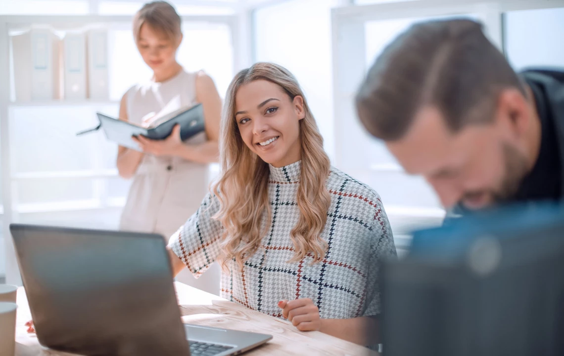 Eine Studentin lernt am Laptop und lächelt in die Kamera.