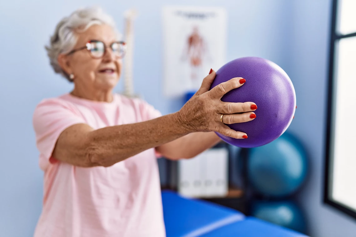 Eine Frau hält einen Ball vor sich bei der Rehabilitationsübung.