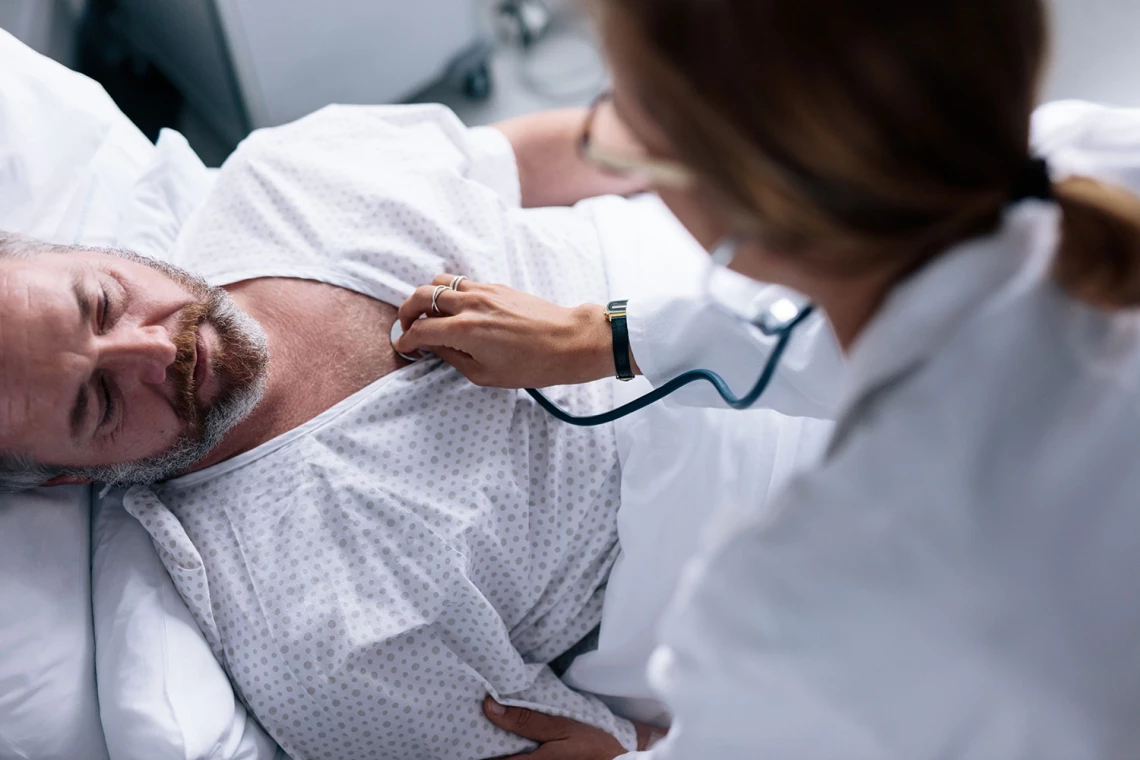 Ein Patient im Bett wird von einer Ärztin mit einem Stethoskop untersucht.
