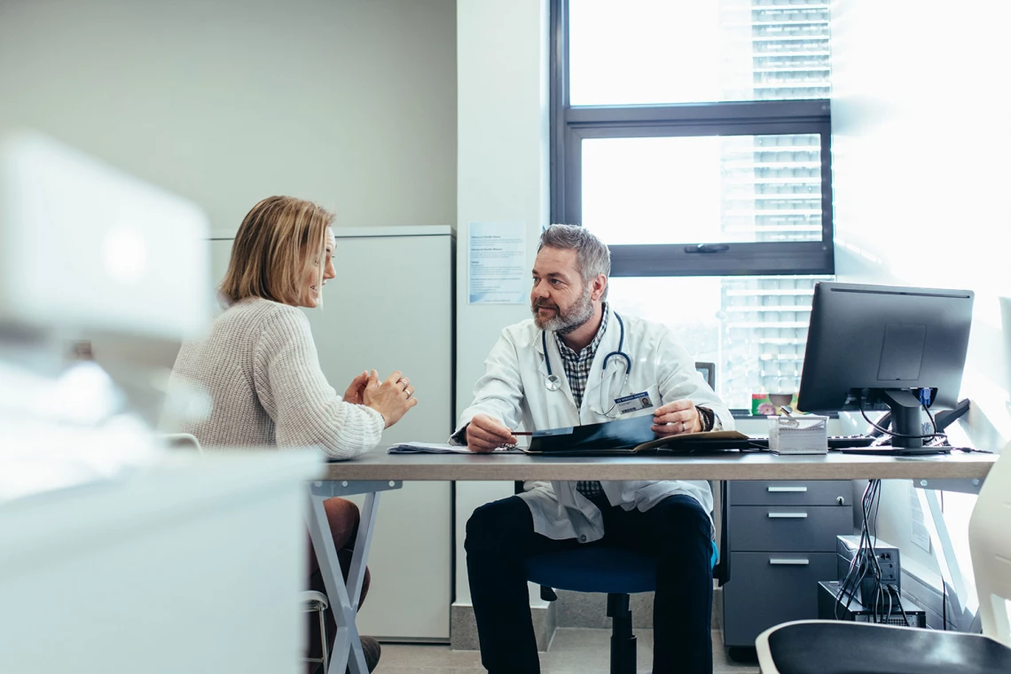 Ein Arzt redet in seinem Büro mit einer Patientin.