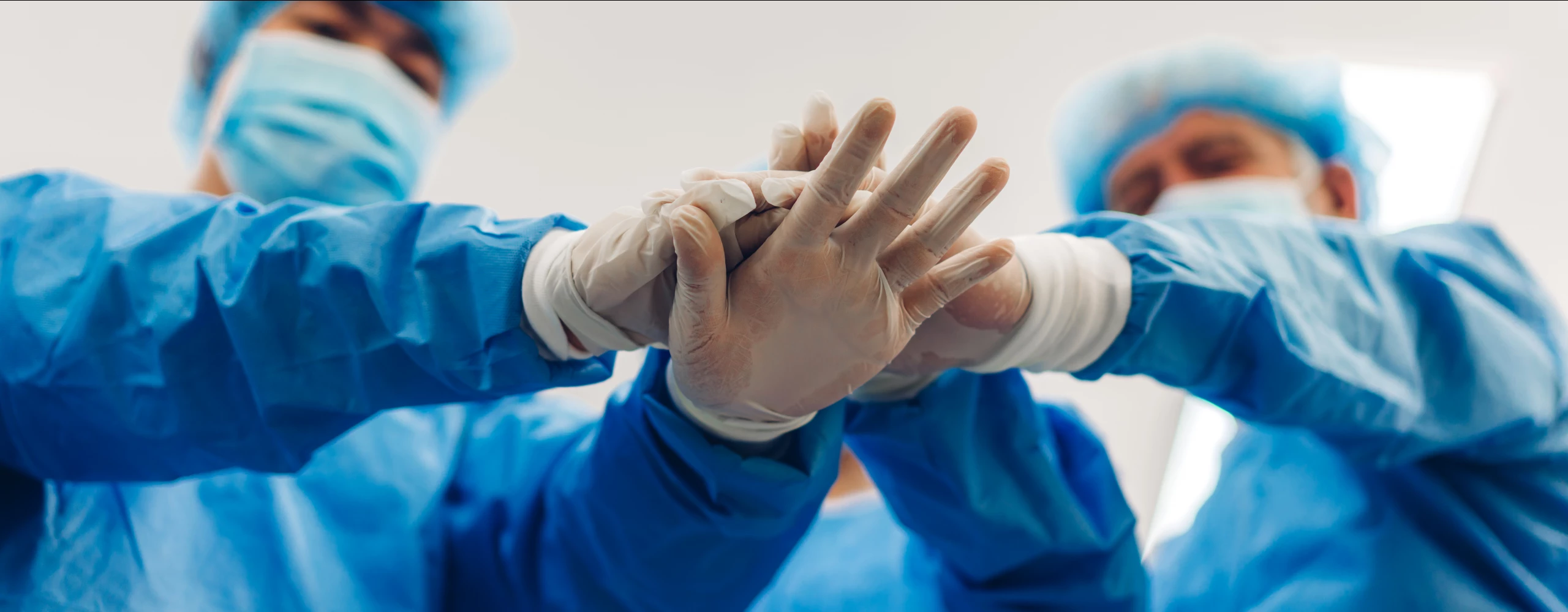 Eine Froschperspektive bei der zwei Ärzte mit Schutzanzügen und Masken die Hände aufeinander halten.