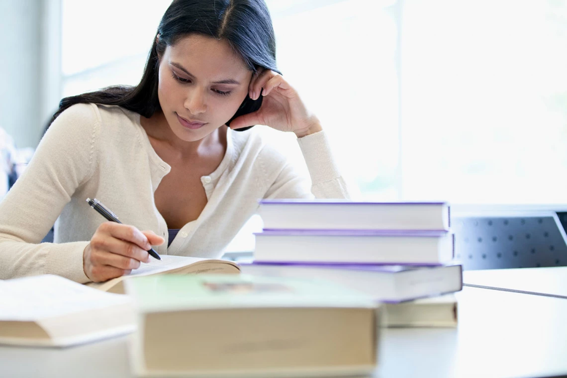 Eine Studentin lernt. Vor ihr liegt ein Bücherstapel auf dem Tisch.